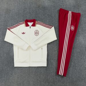 Chándal España 26/27 Clean extendido con chaqueta crema, escudo de España, logotipo del trébol y pantalón granate con franjas blancas
